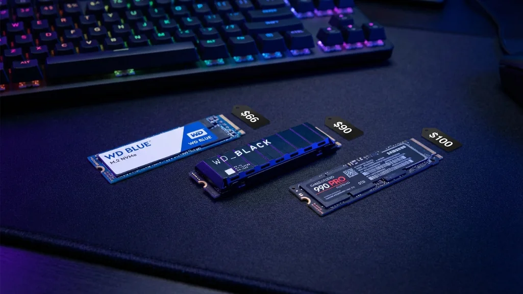 Budget gaming SSDs comparison showing WD Blue SN5000, WD Black SN7100, and Samsung 990 EVO Plus on gaming desk