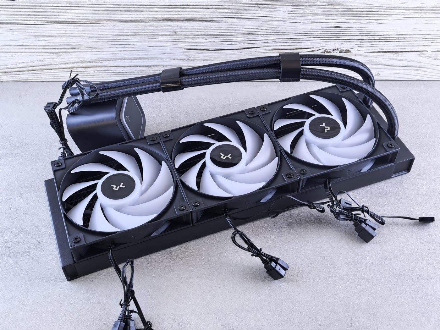 360mm AIO liquid cooler with three white-lit 120mm fans on the radiator, braided tubes and the pump block, laid out on a grey surface