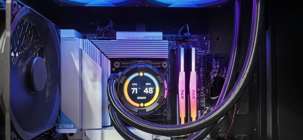 Inside a gaming PC: an AIO pump block with a round temperature display mounted on the CPU socket, braided tubes running to a top-mounted radiator, with the motherboard VRM heatsinks around the socket