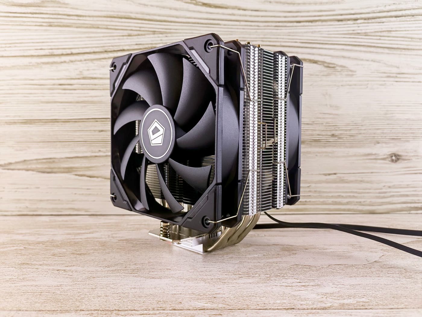 Dual-tower air CPU cooler with two black 120mm fans, nickel-plated heatsink fins and heatpipes, standing on a light wooden surface