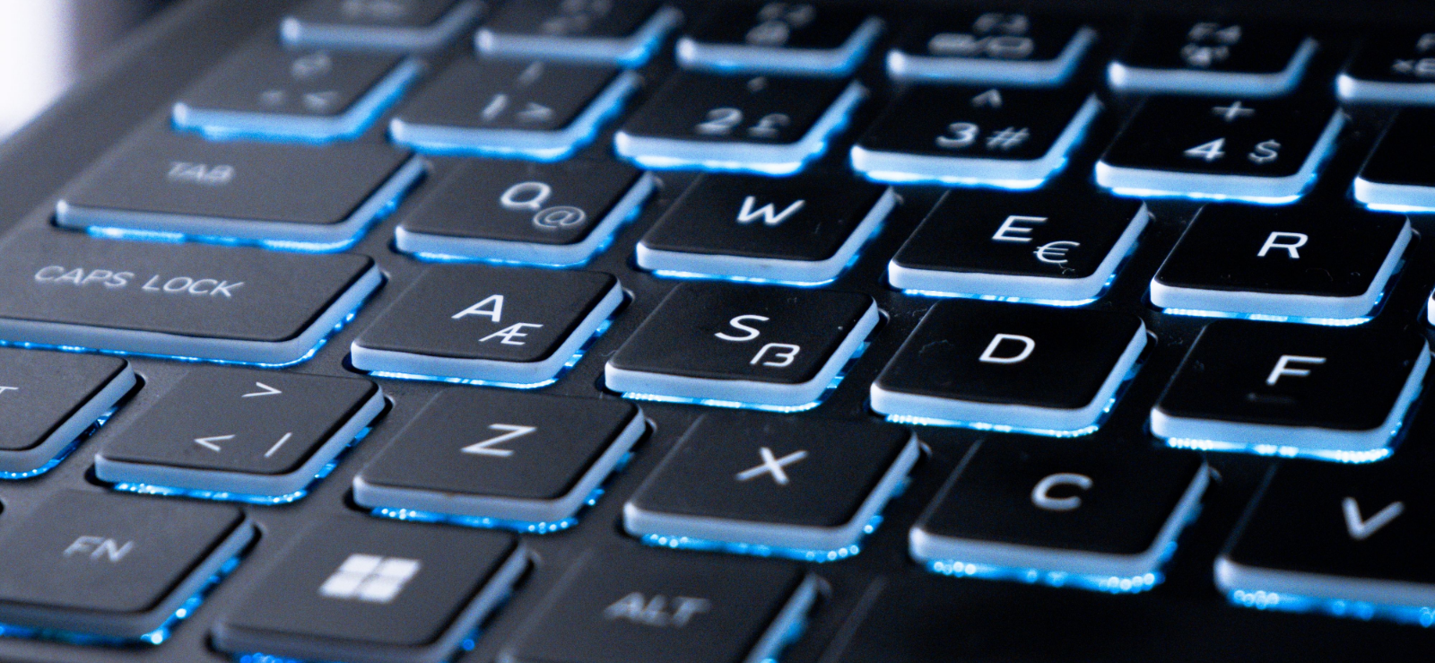 Close-up of a gaming laptop's blue backlit keyboard with the screen glowing behind it